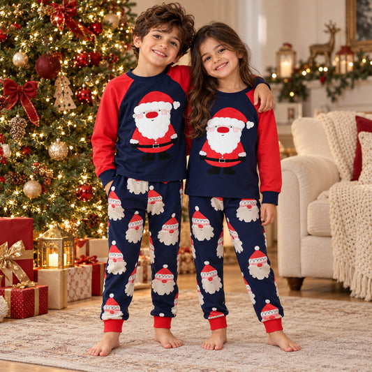Boy and girl wearing matching navy and red cotton Santa Christmas pajamas beside decorated tree