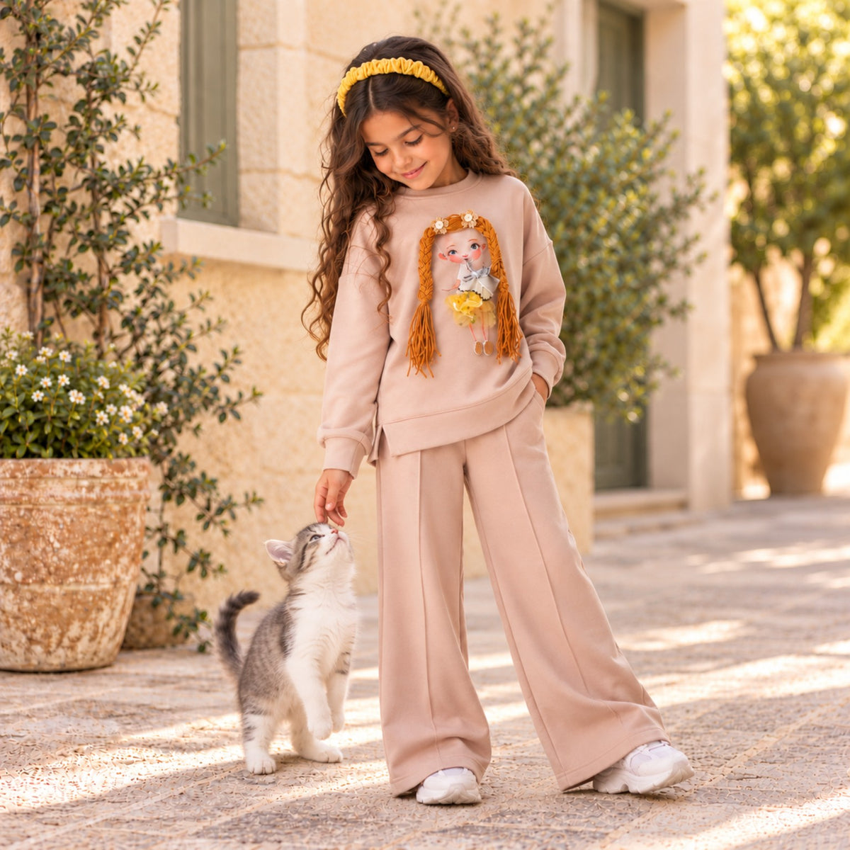 Girl wearing beige doll-print two-piece outfit, outdoors with a kitten