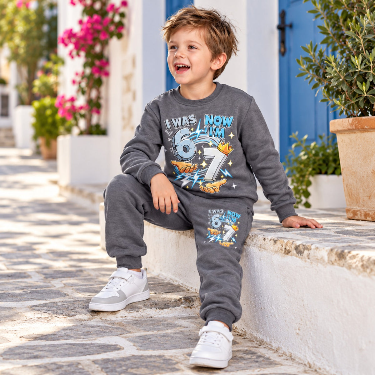 Boy sitting outdoors in grey I Was 6 Now I'm 7 sweatshirt and printed joggers