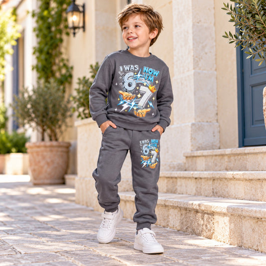 Boy modelling grey I Was 6 Now I'm 7 birthday sweatshirt and matching joggers, full-length standing view